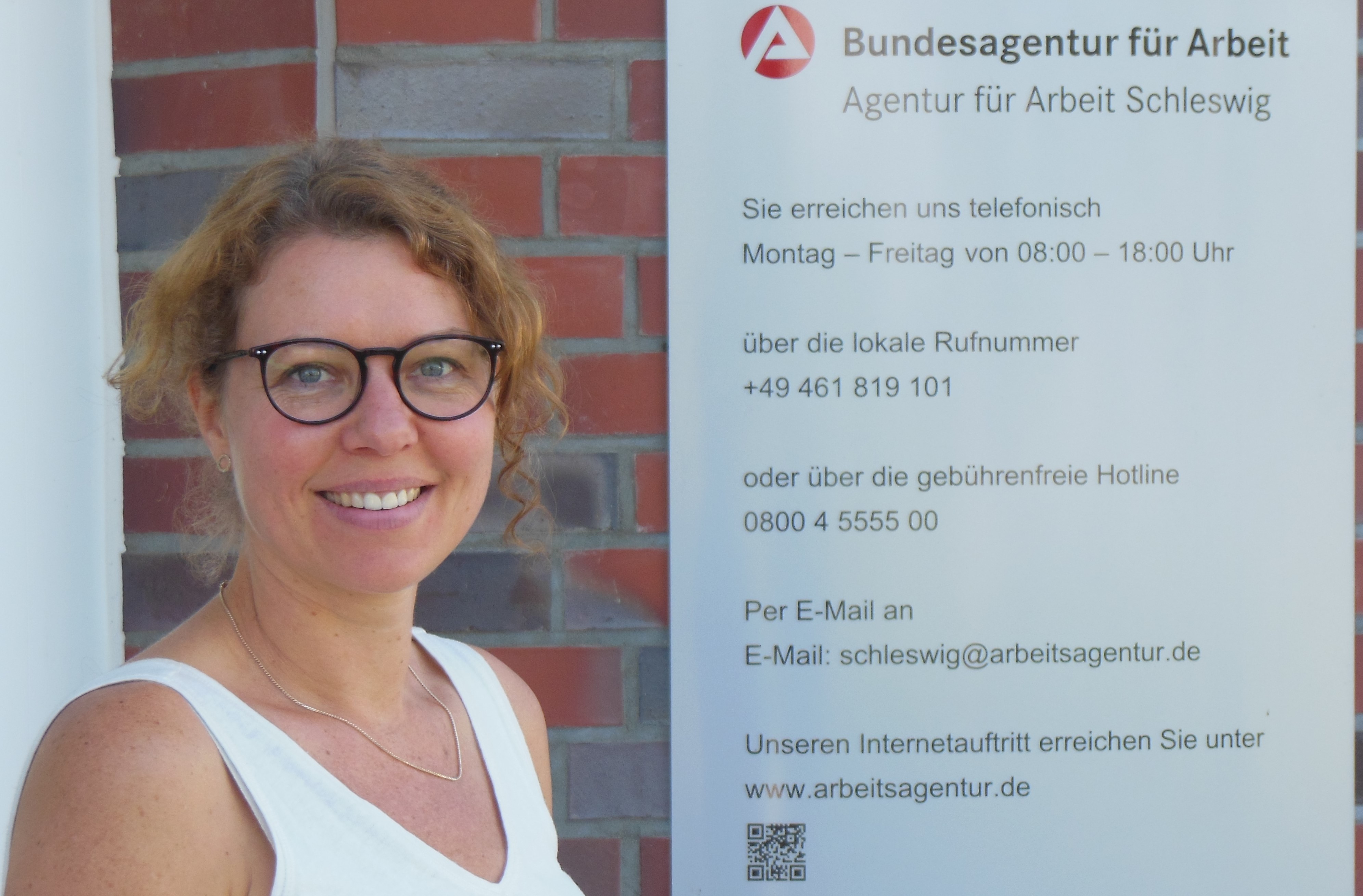 Frau Fries vor der AA Schleswig mit Schild zu den Öffnungszeiten