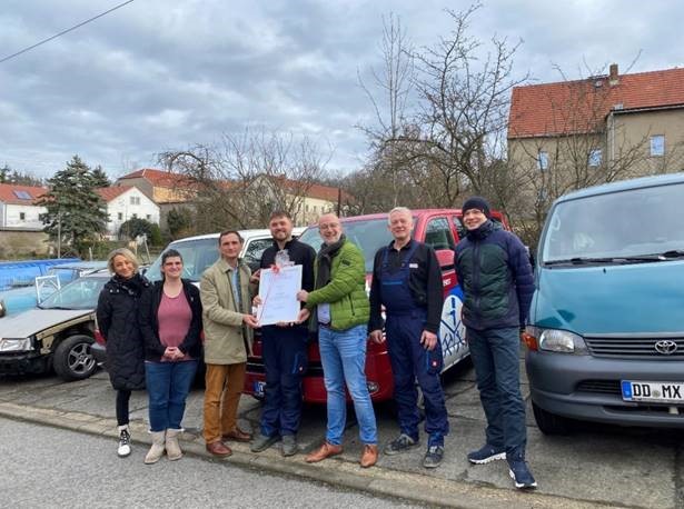 5 Männer und 2 Frauen vor Autos bei der Überreichung eines Inklusionszertifikates