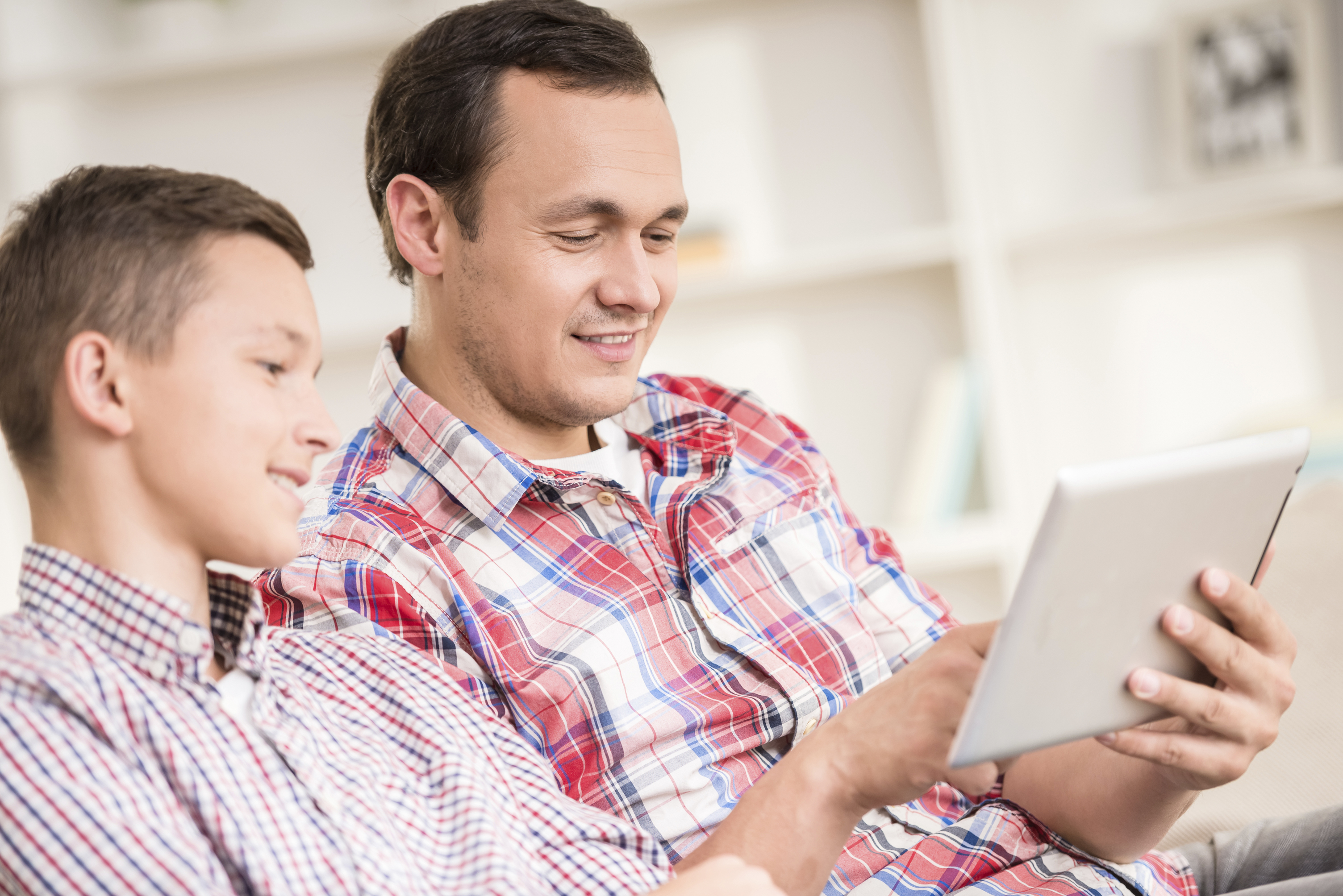 Ein Vater und sein Sohn sitzen zu Hause und schauen auf ein Tablet