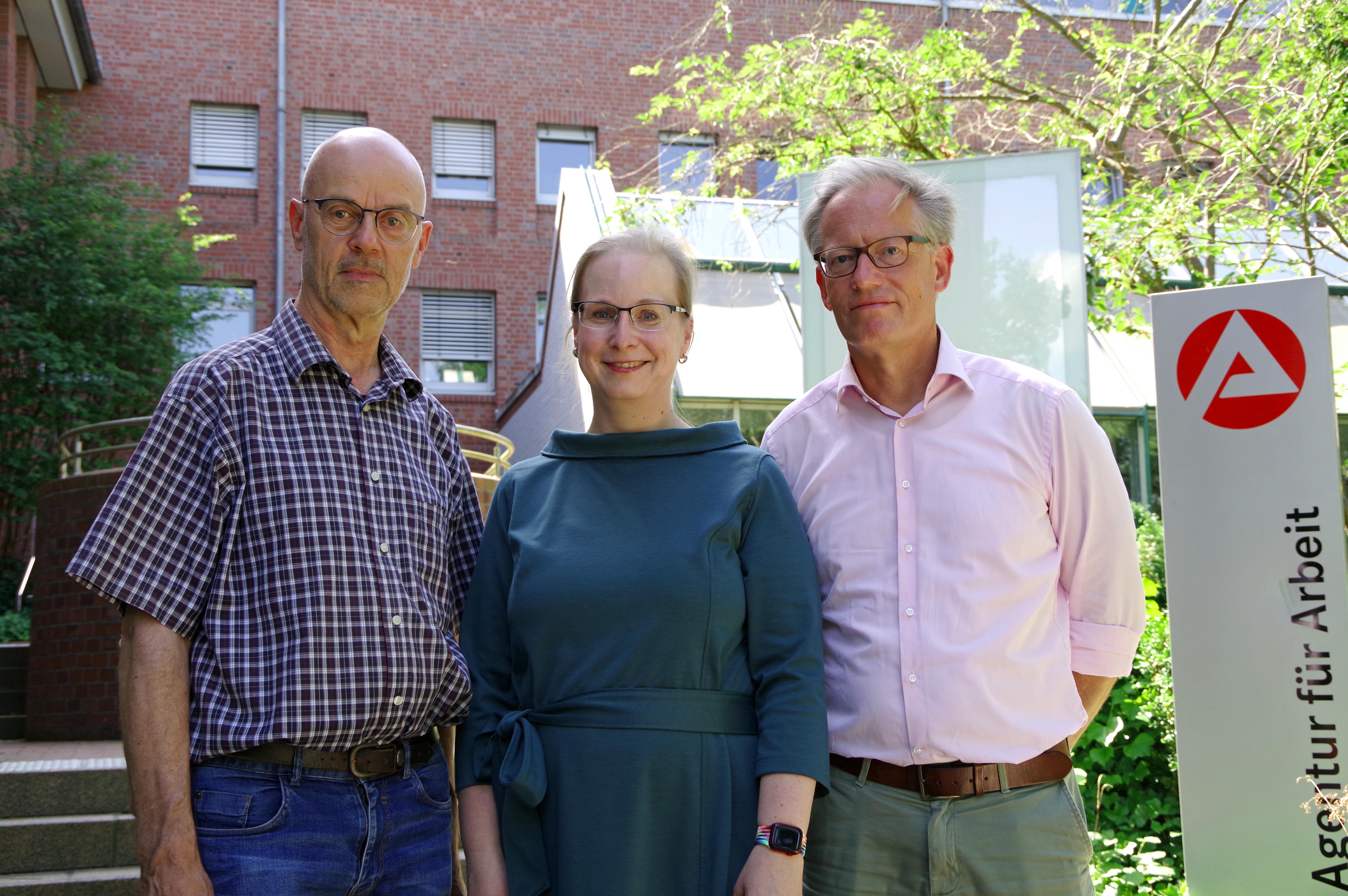 Joachim Sauer, Kathleen Wieczorek und Dirk Polchow stehen auf einer Trepper vor der Agentur für Arbeit Bad Oldesloe und lächeln in die Kamera