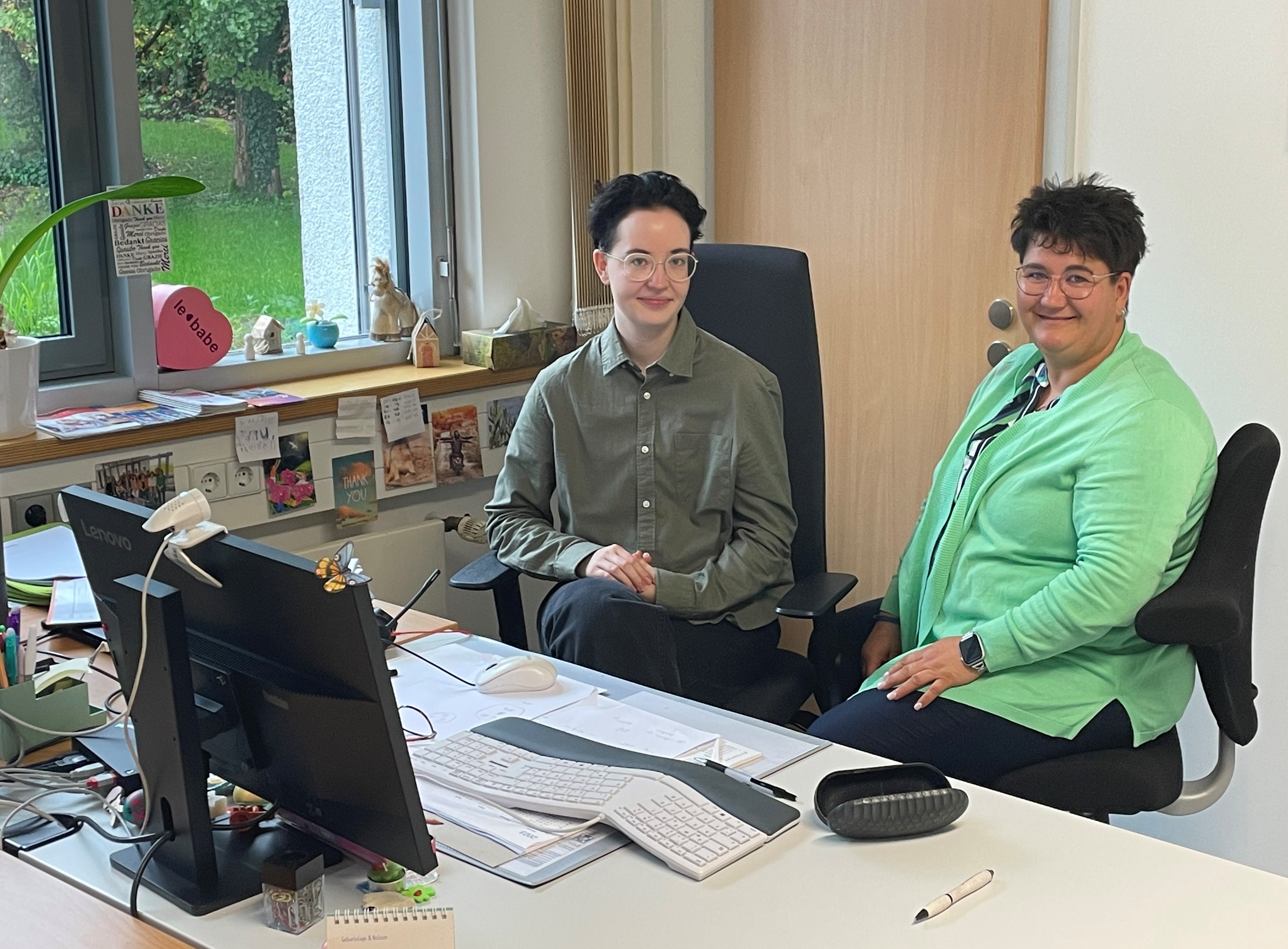 Auf diesem Bild sitzen Frau Frölich und Frau Bauer gemeinsam am Schreibtisch