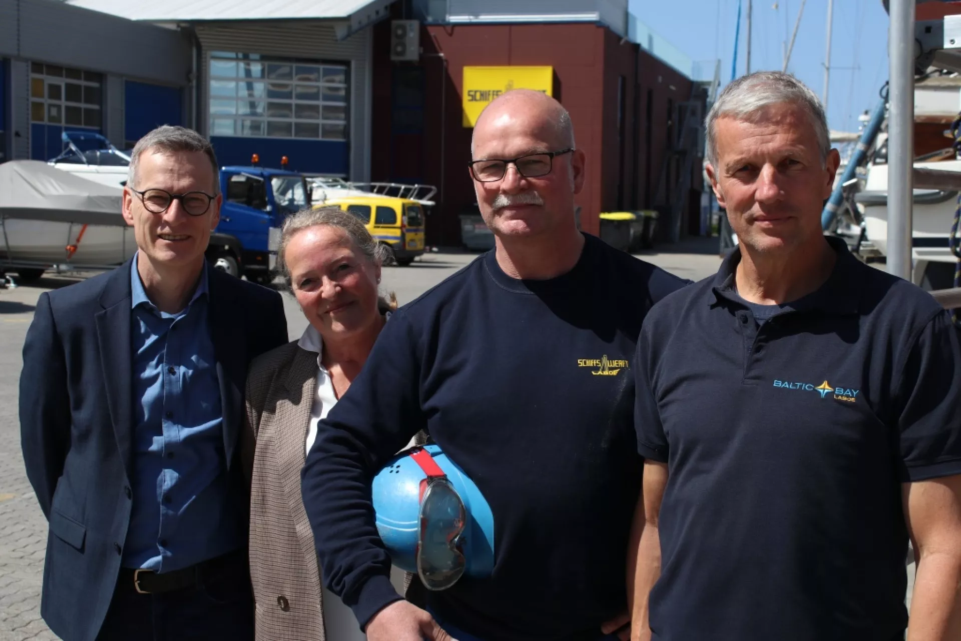 Herr Rump, Frau Linnig, Herr Komm und Herr Gürke vor den Gebäuden der Schiffswerft Laboe