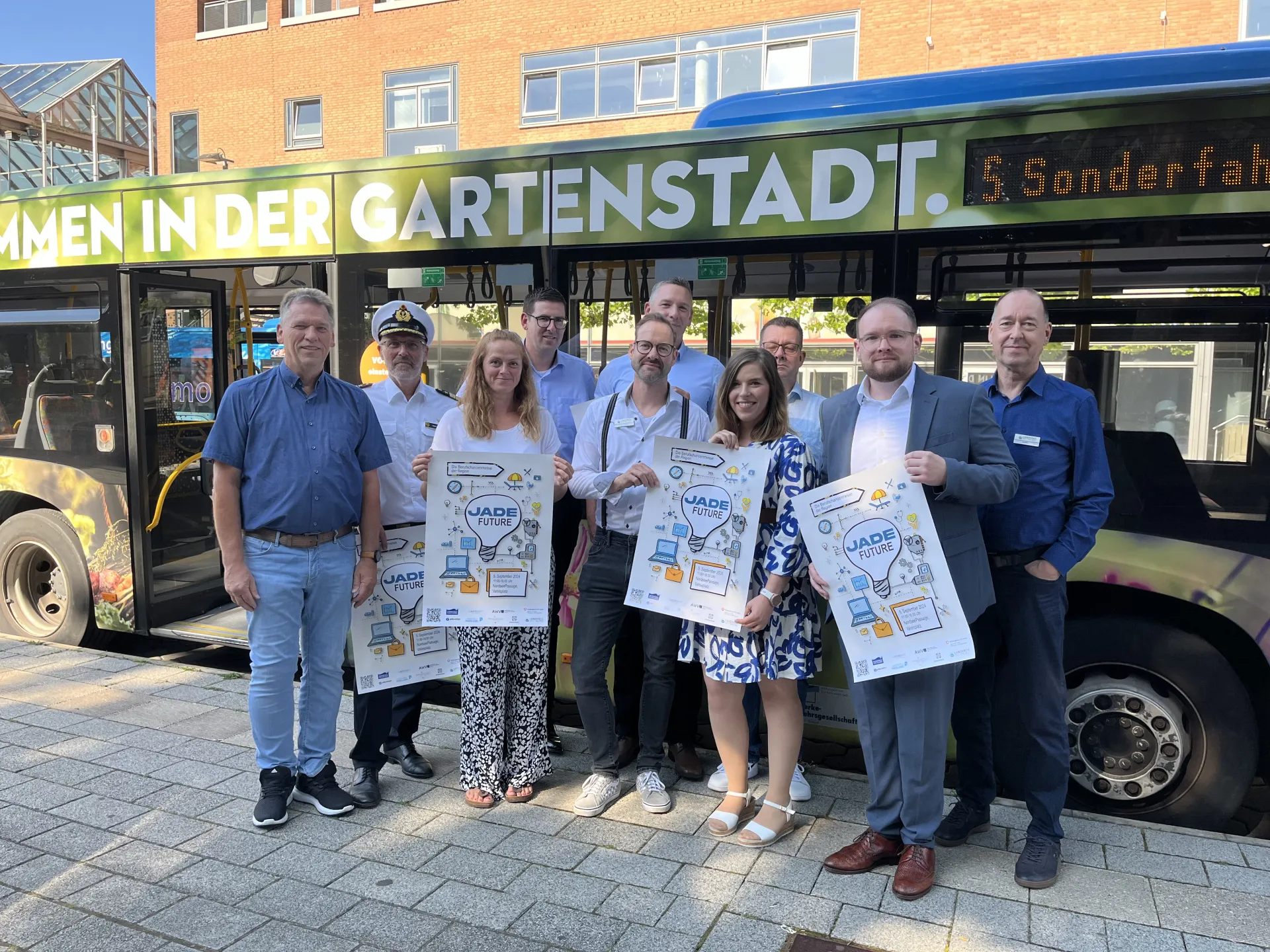 Personen stehen mit Plakaten der Berufsmesse JadeFuture vor einem Linienbus