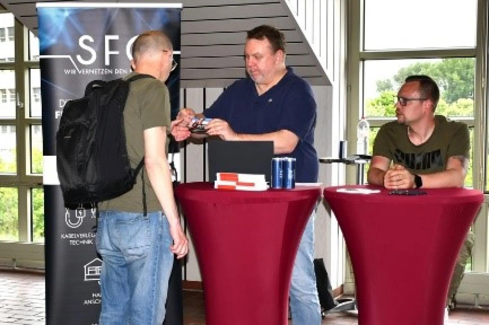 Zwei Mitarbeiter einer Firma stehen an zwei Stehtischen und beraten einen Interessierten