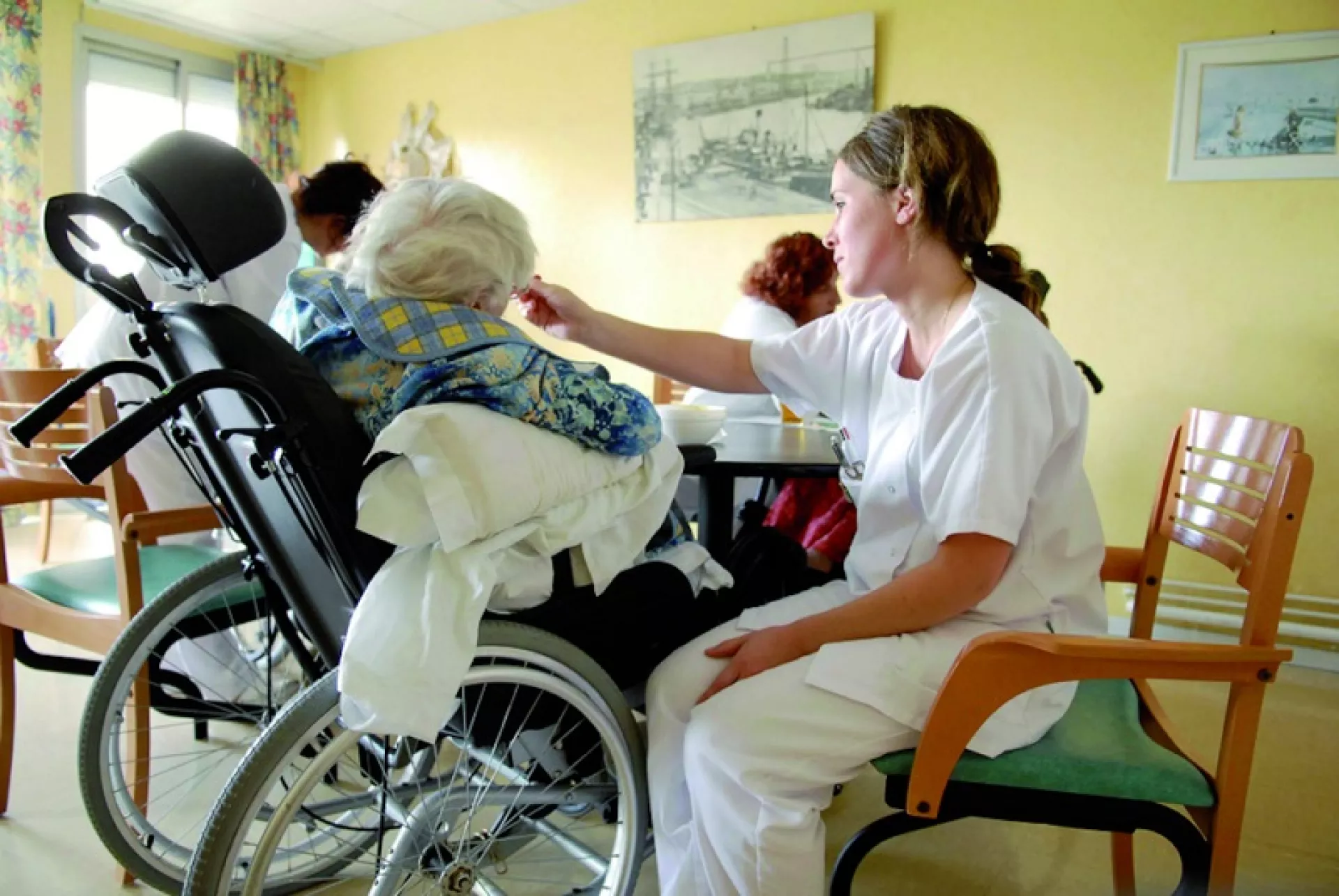 Eine Altenpflegerin füttert eine alte Frau im Rollstuhl