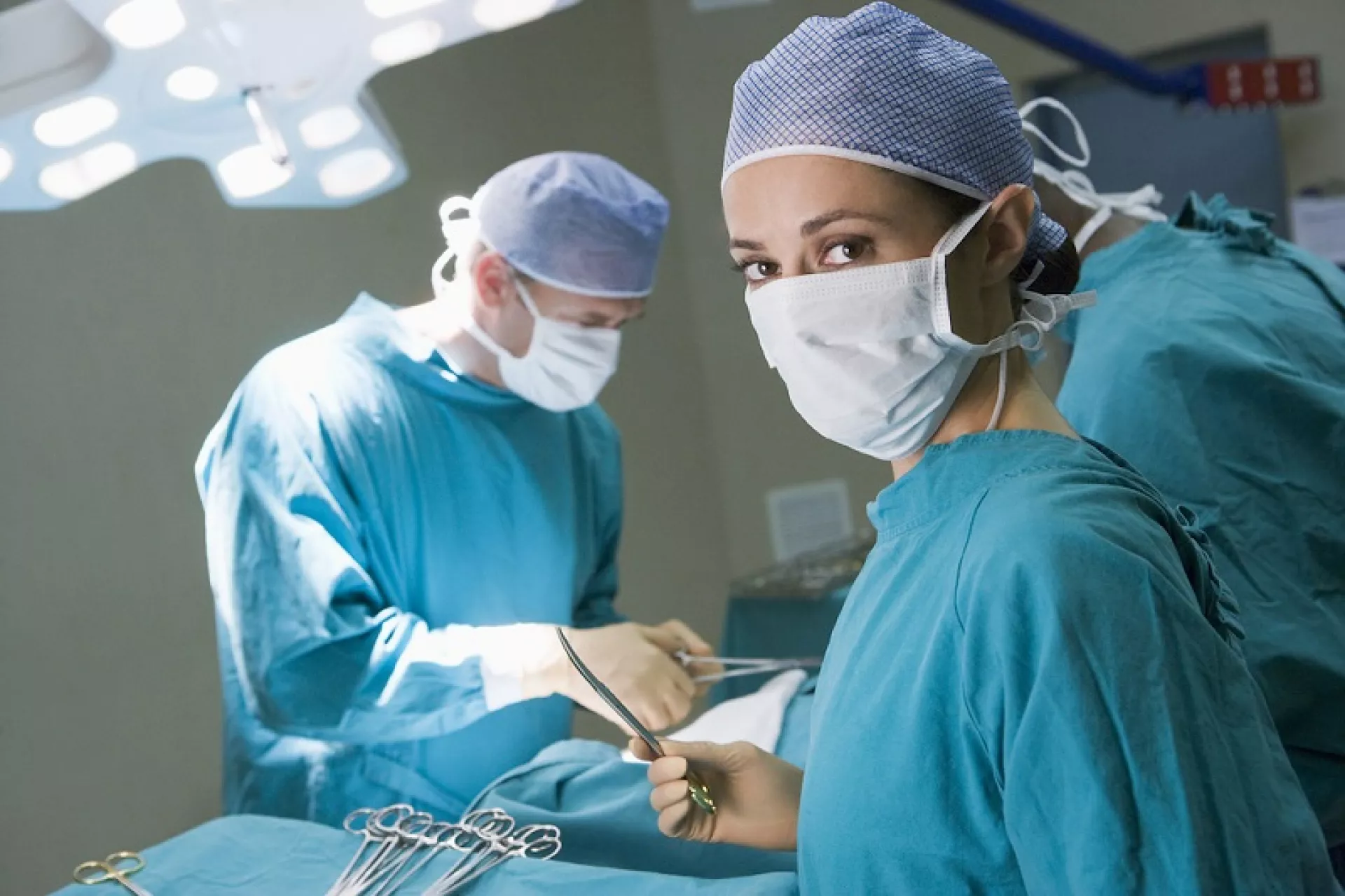 Eine Ärztin und zwei Äzte mit Mundschutz und OP-Kitteln bei einer Operation.