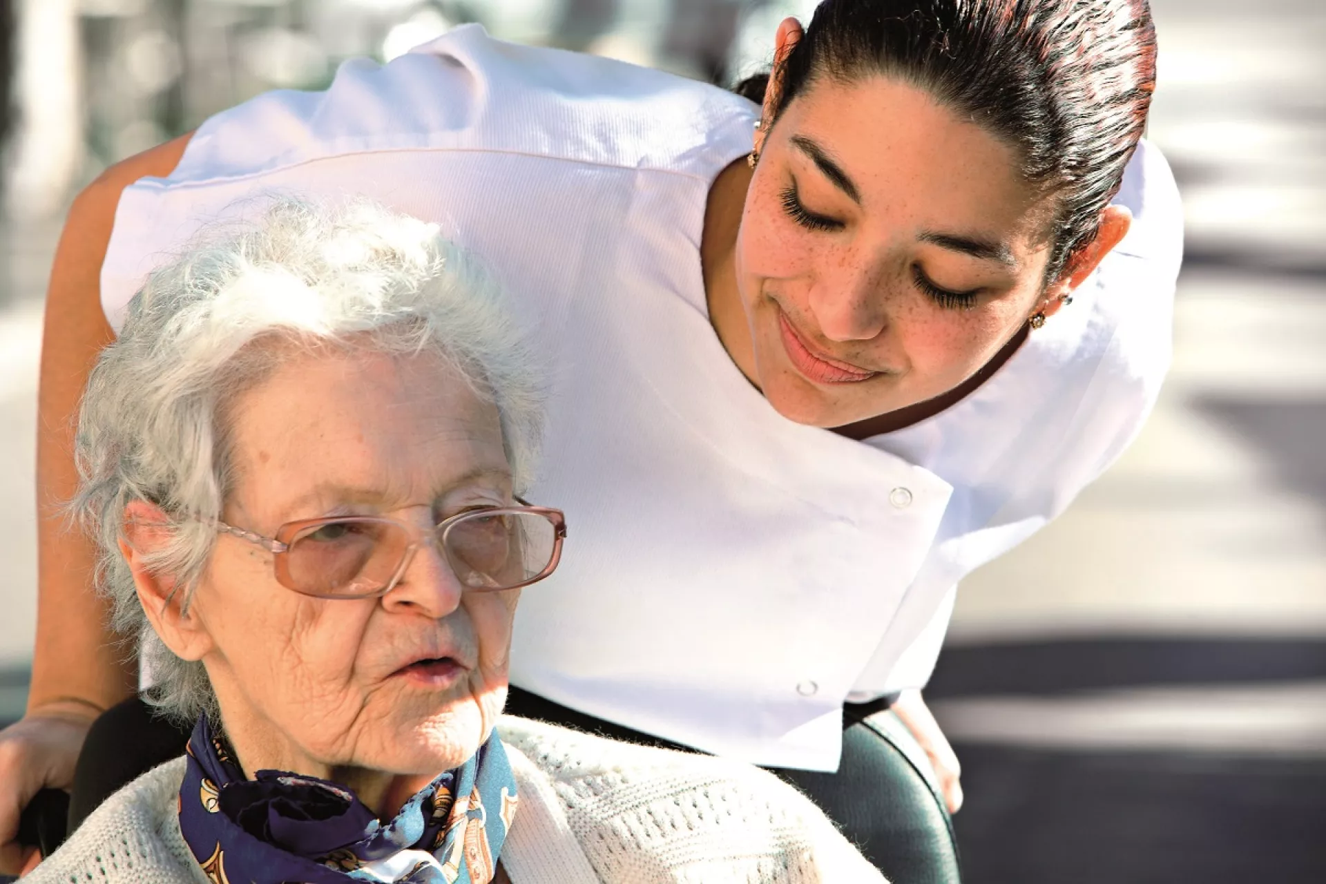 Pflegerin beugt sich über sitzende Seniorin