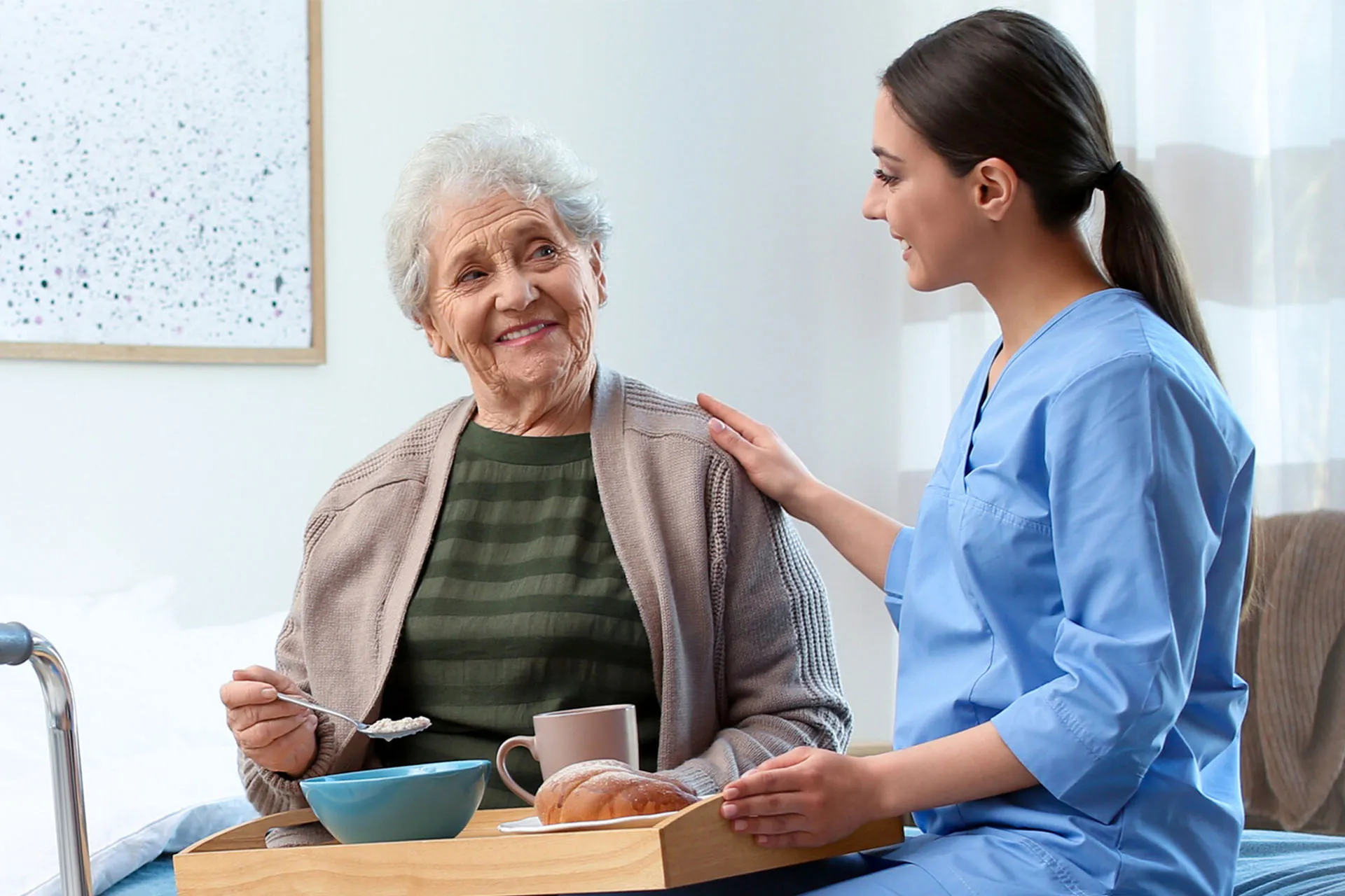 Pflegekraft sitzt mit Bewohnerin auf dem Bett