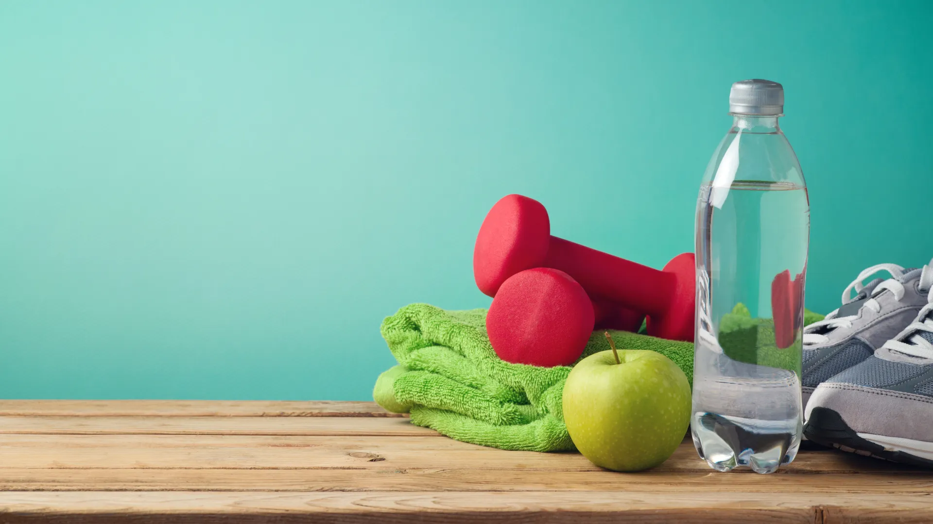 Sportschuhe, Handtuch, Hanteln und ein Apfel und eine Flache Wasser auf Holzbank