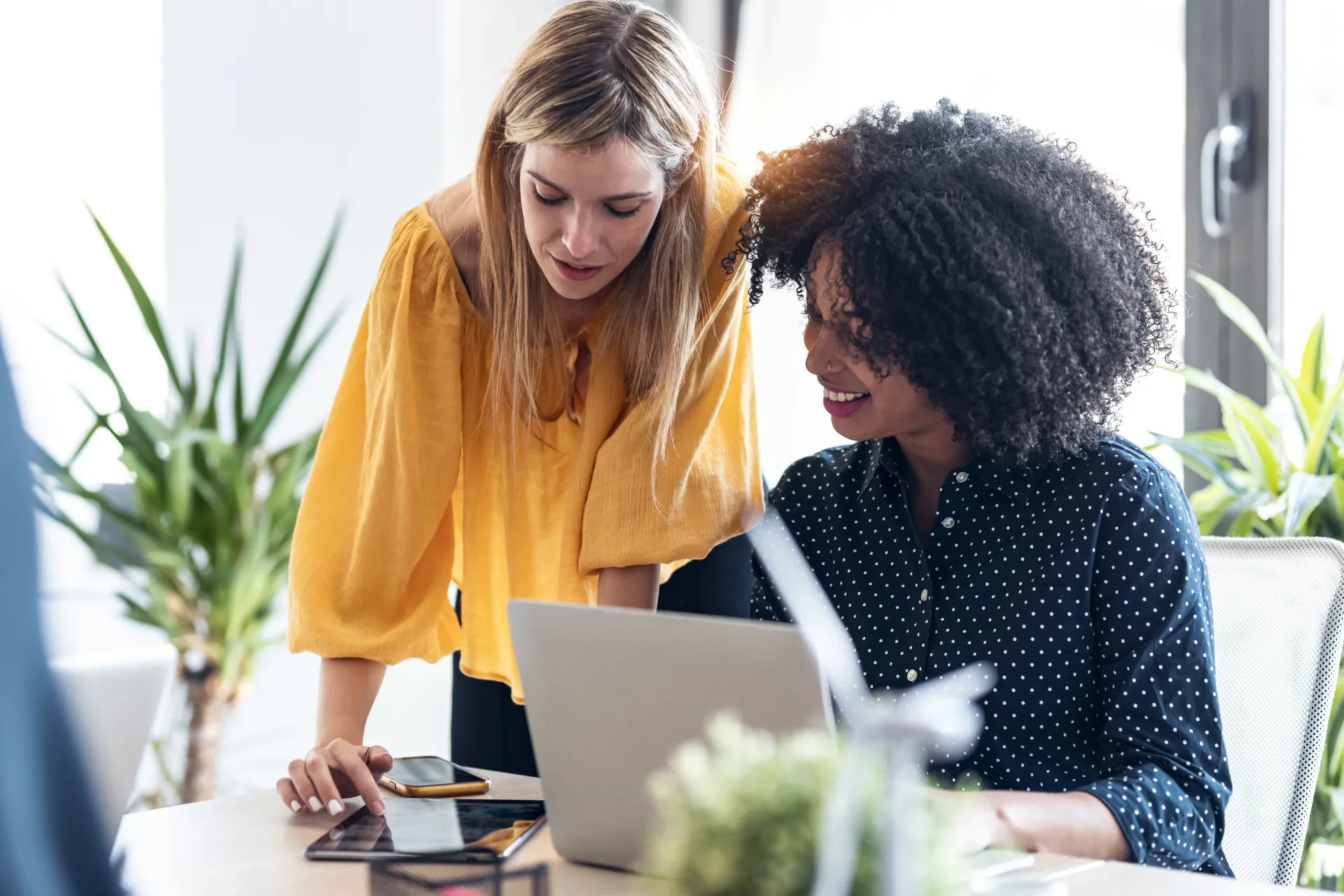 Zwei Geschäftsfrauen arbeiten gemeinsam mit Laptop, Tablet und Smartphone im Büro