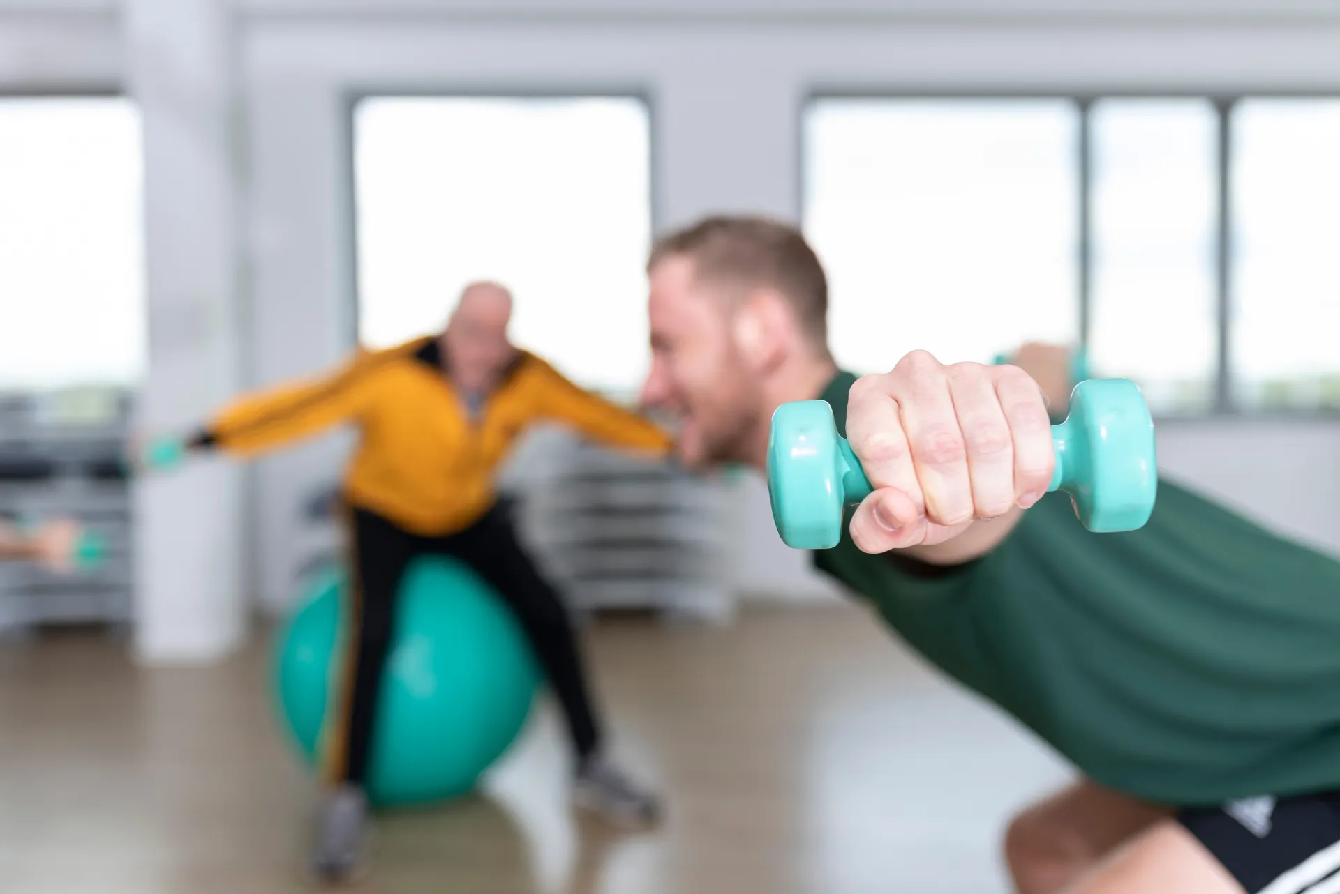 Person trainiert mit Hanteln unter Anleitung eins Personaltrainers im Hintergrund