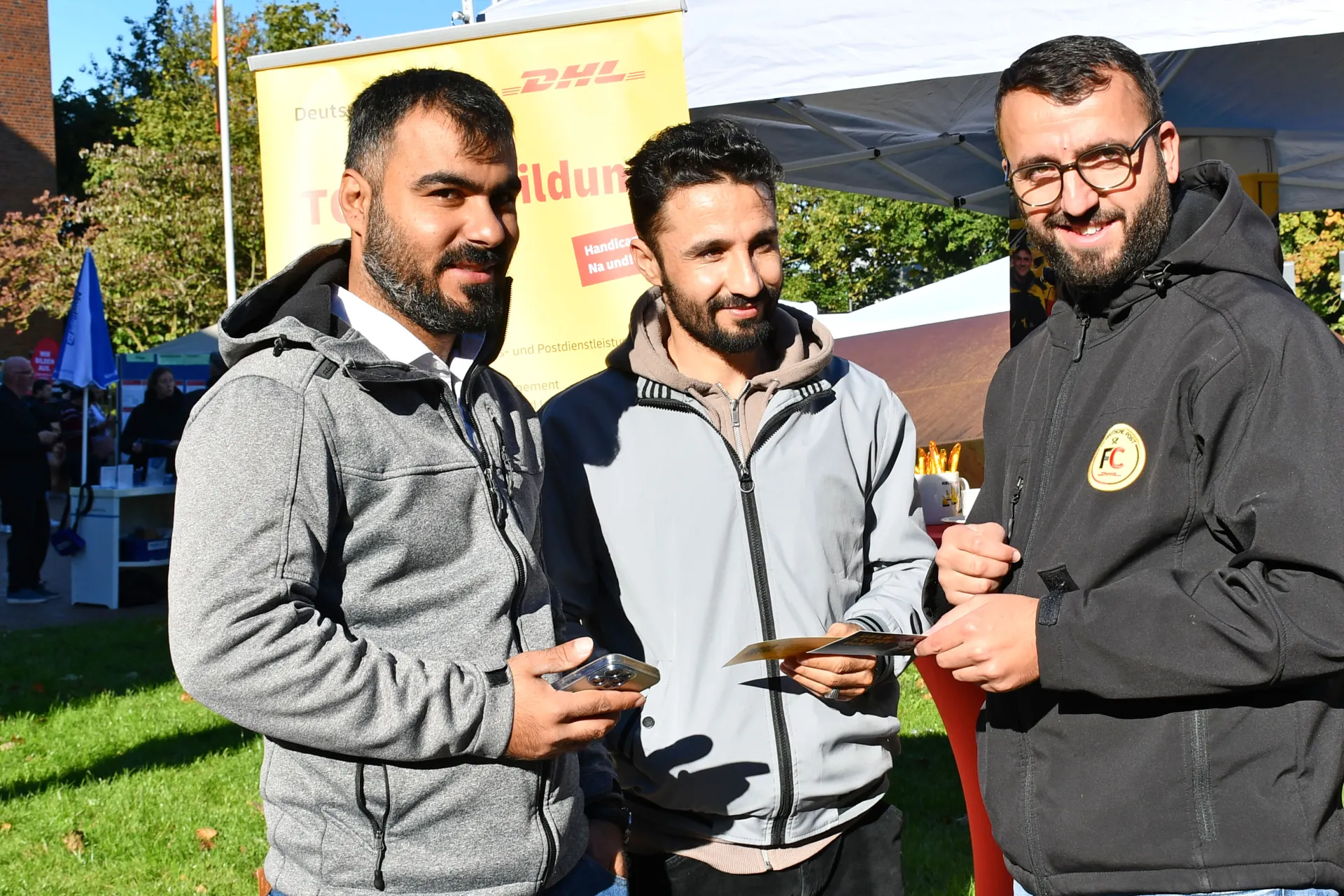 Drei junge Männer stehen vor einem Messeplakat