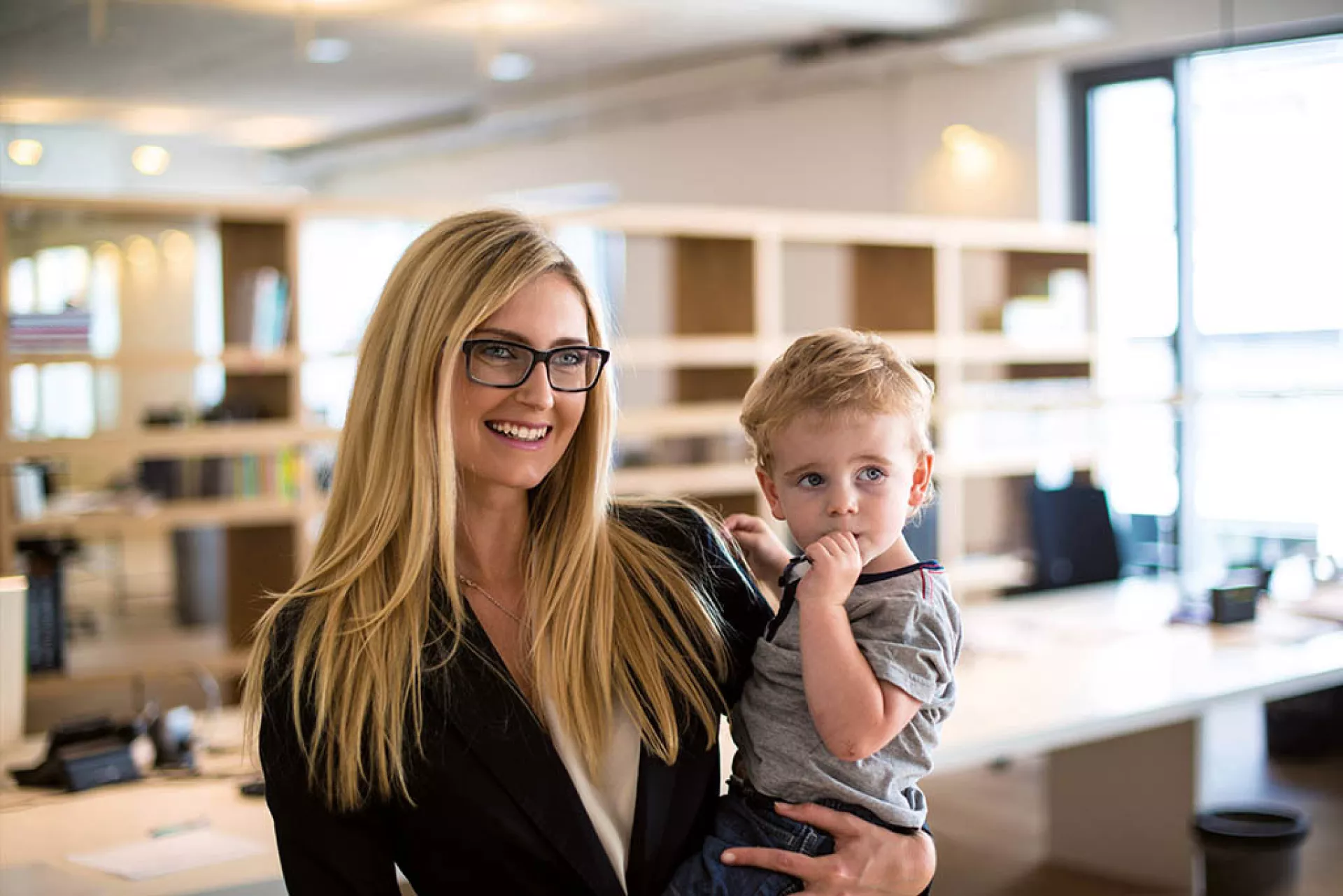 Junge Frau mit ihrem Kind auf dem Arm in einem Großraum-Büro
