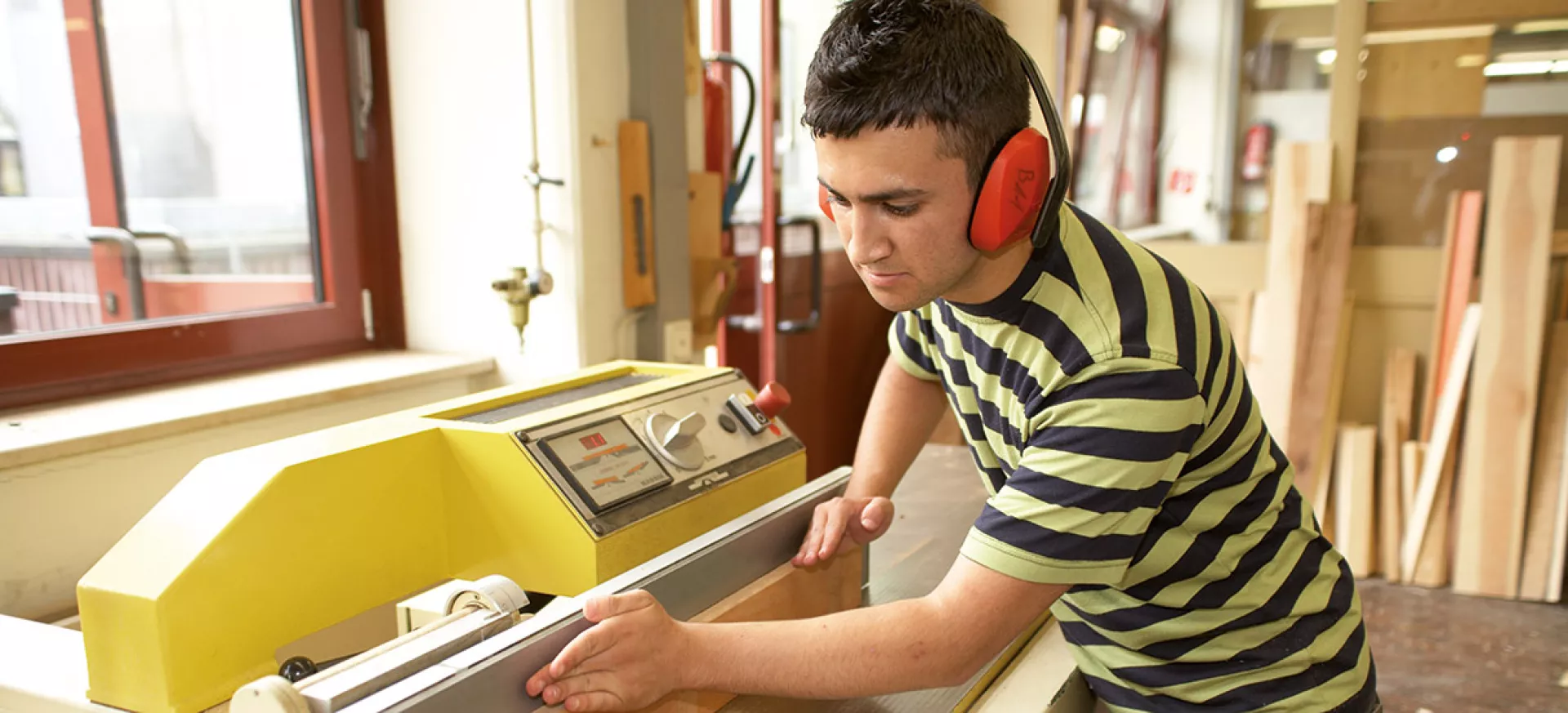 Junger Mann mit Gehörschutz an einer Holzbearbeitungsmaschine in einer Schreinerei
