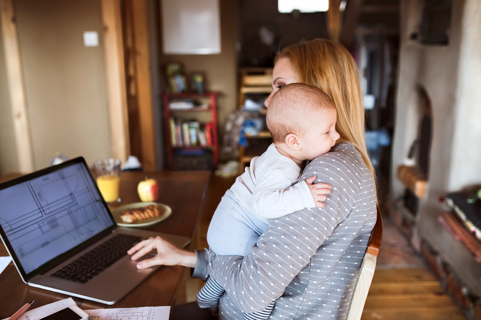 Frau mit Baby im Arm arbeitet zuhause am Laptop