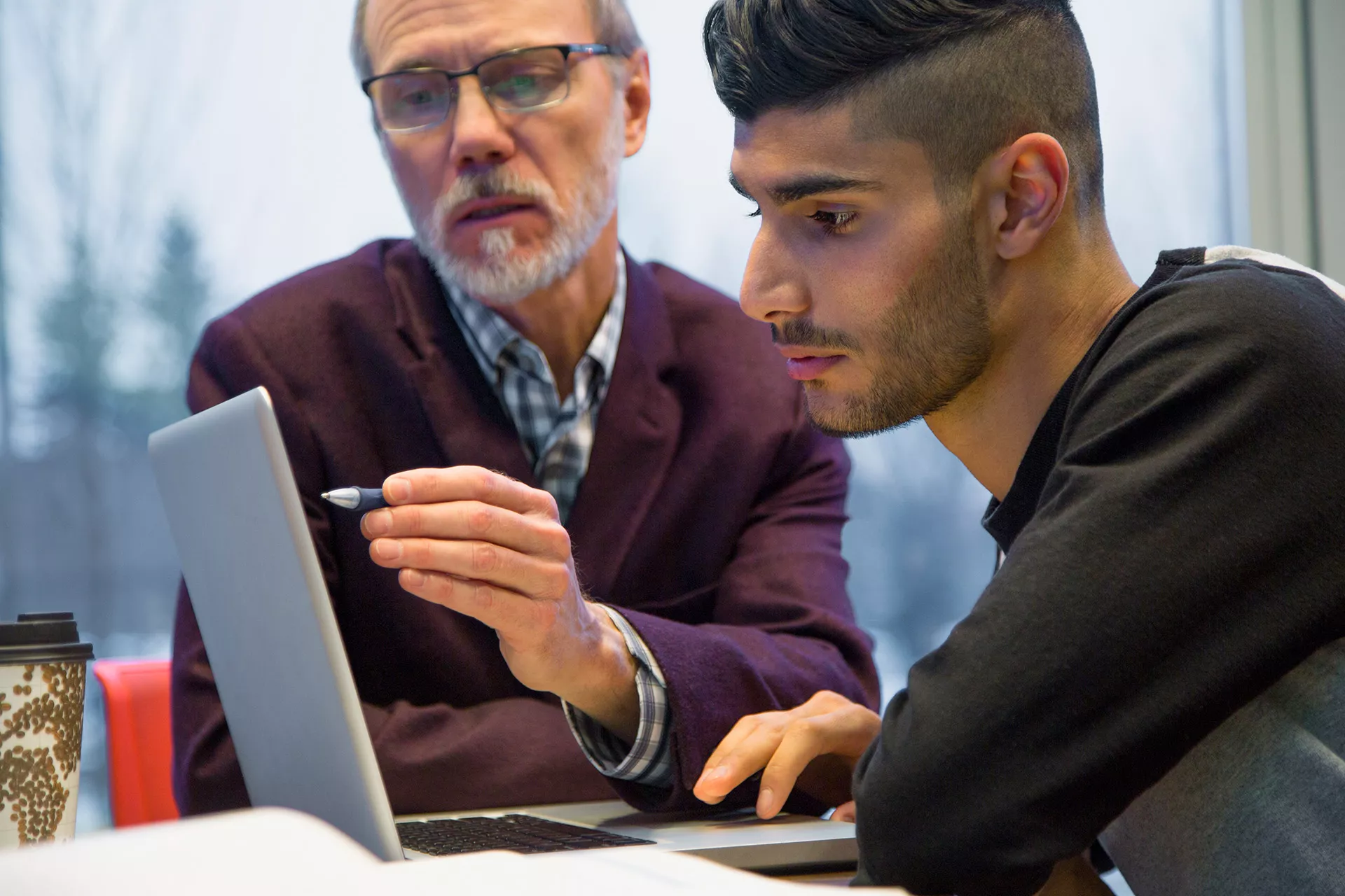 Älterer Mann erklärt Jugendlichem etwas auf dem Laptop-Bildschirm