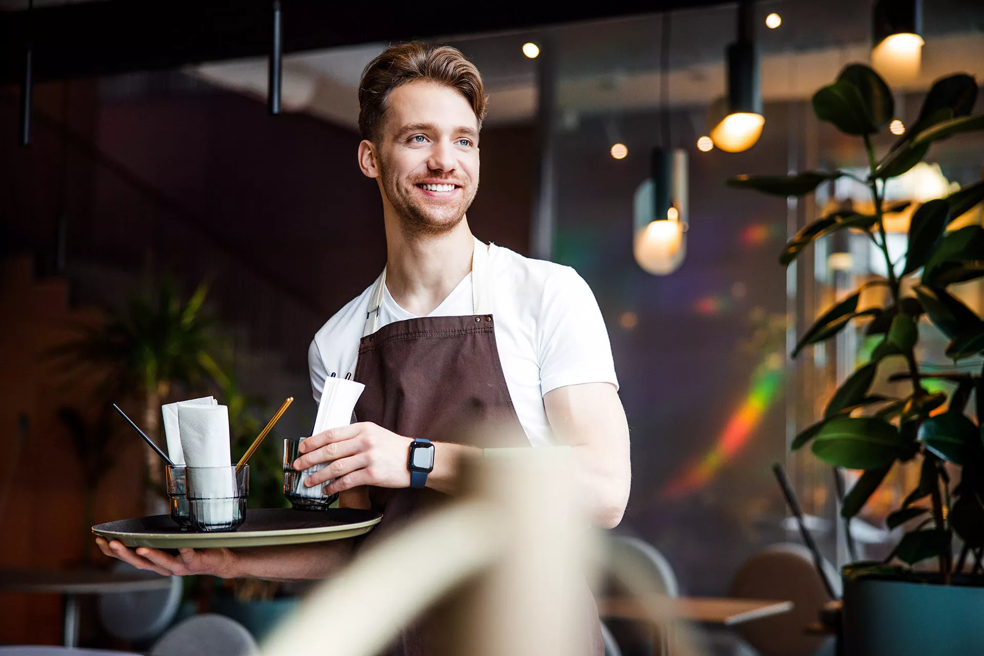 Junger Mann arbeitet als Kellner in einem Cafe und trägt ein Tablett