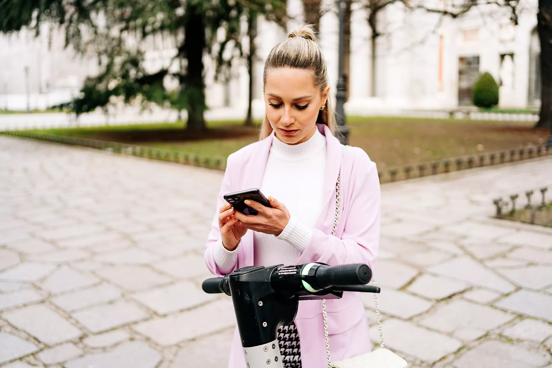 Elegante junge Frau steht mit e-Roller auf Straßenkreuzung und schaut auf ihr Tablet