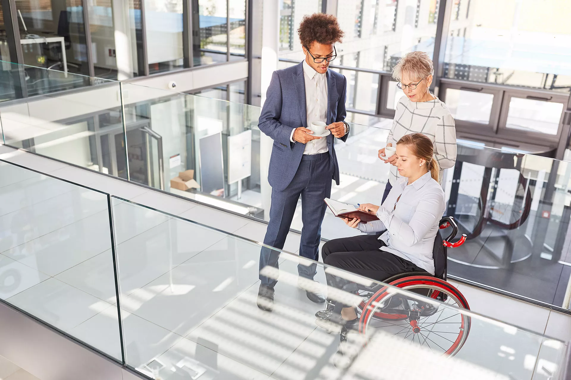 Eine Frau im Rollstuhl spricht in einem Büroflur mit einem Kollegen und einer Kollegin