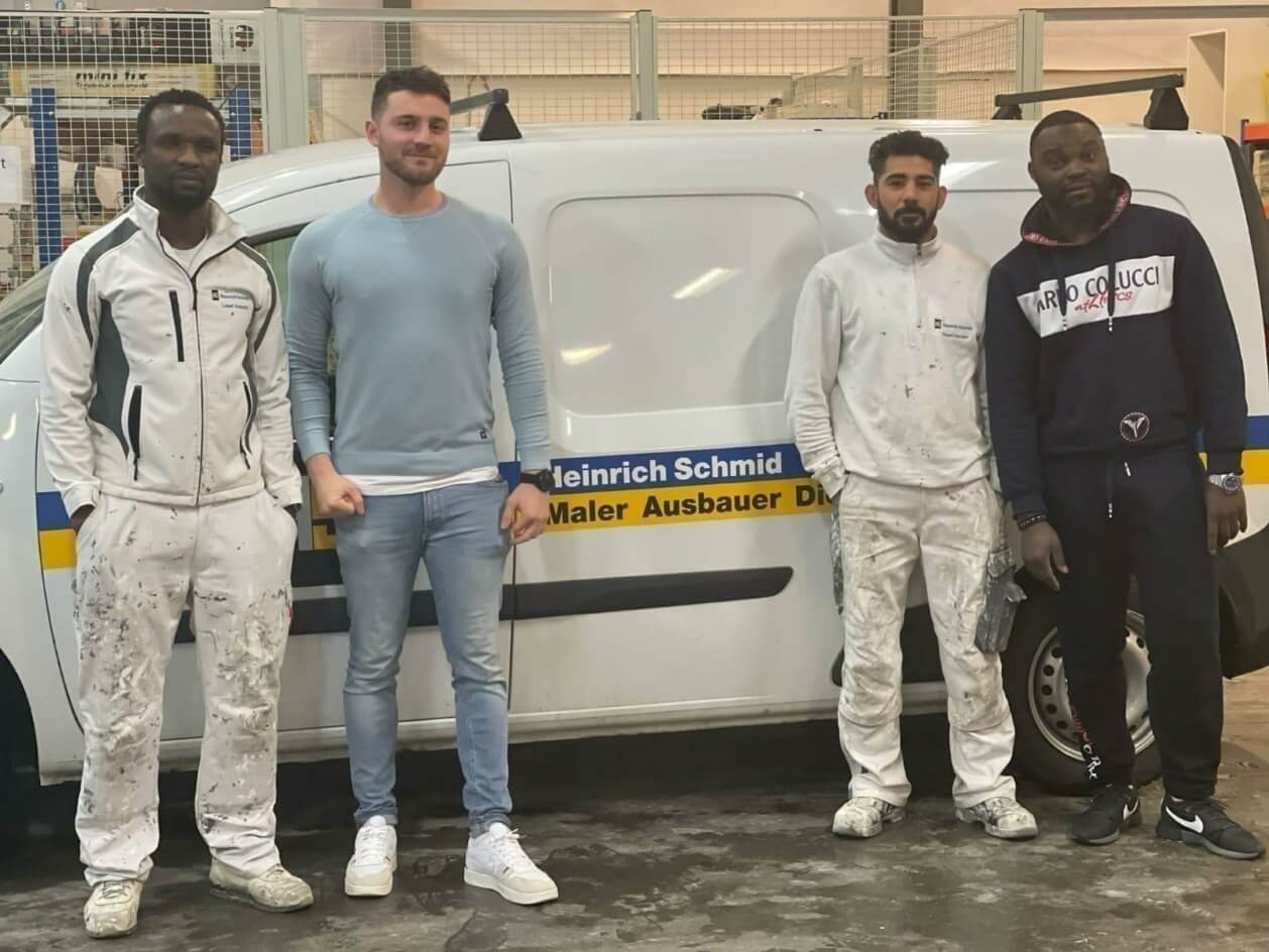 Marc Kwasniok steht mit drei Azubis vor einem Firmenauto