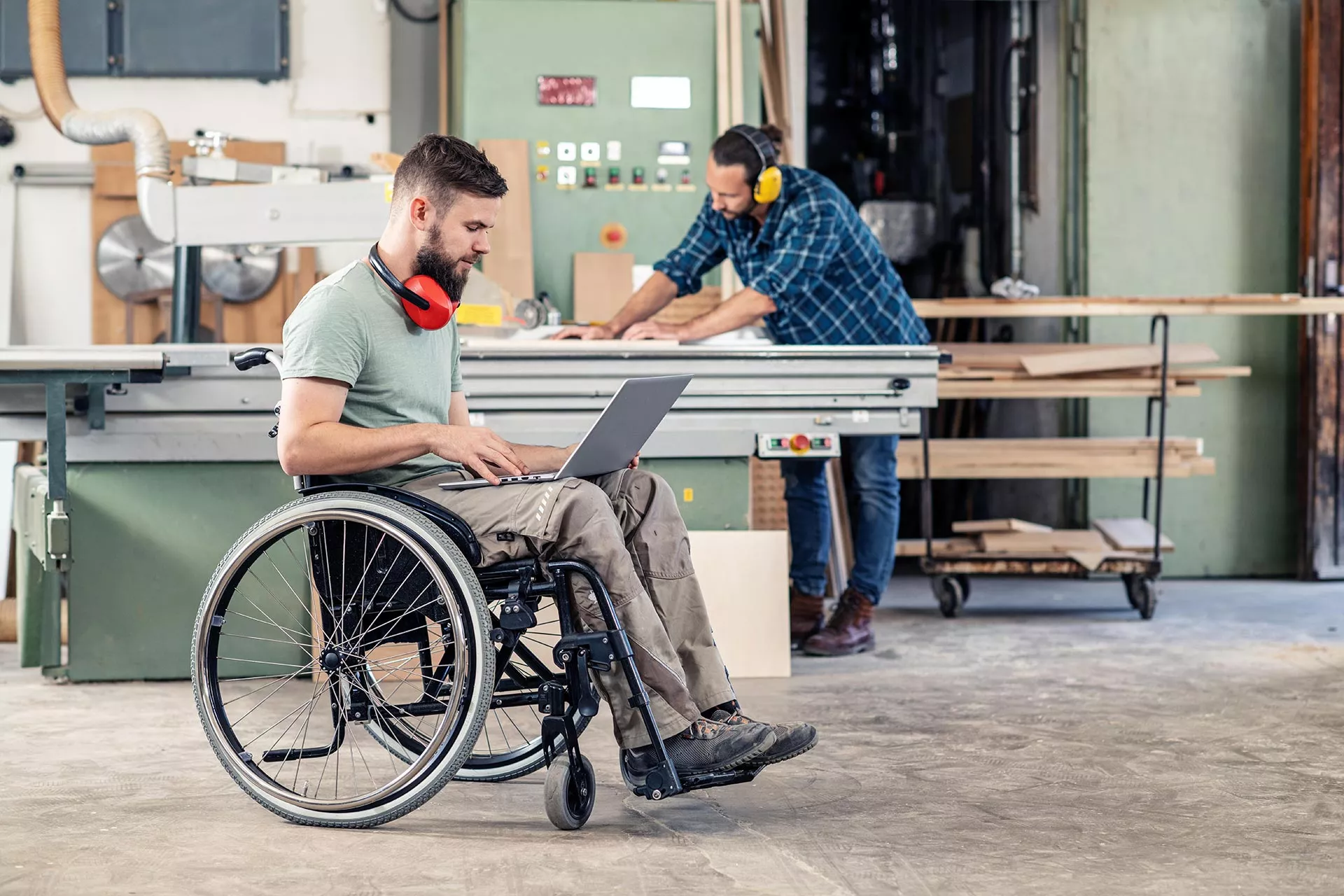 Ein junger Mann im Rollstuhl arbeitet in einer Werkstatt am Laptop