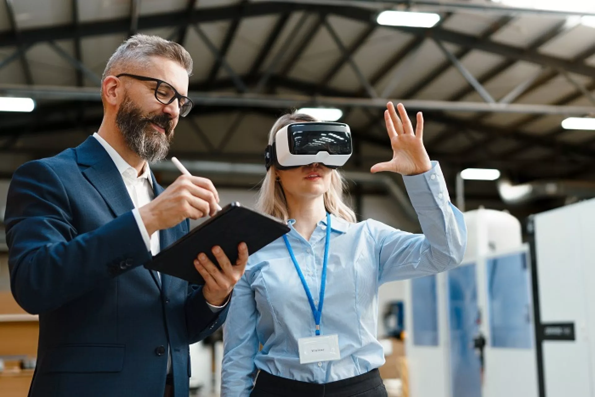 Junge Frau testet eine VR-Brille. Neben ihr steht ein Mann mit Tablet in der Hand.