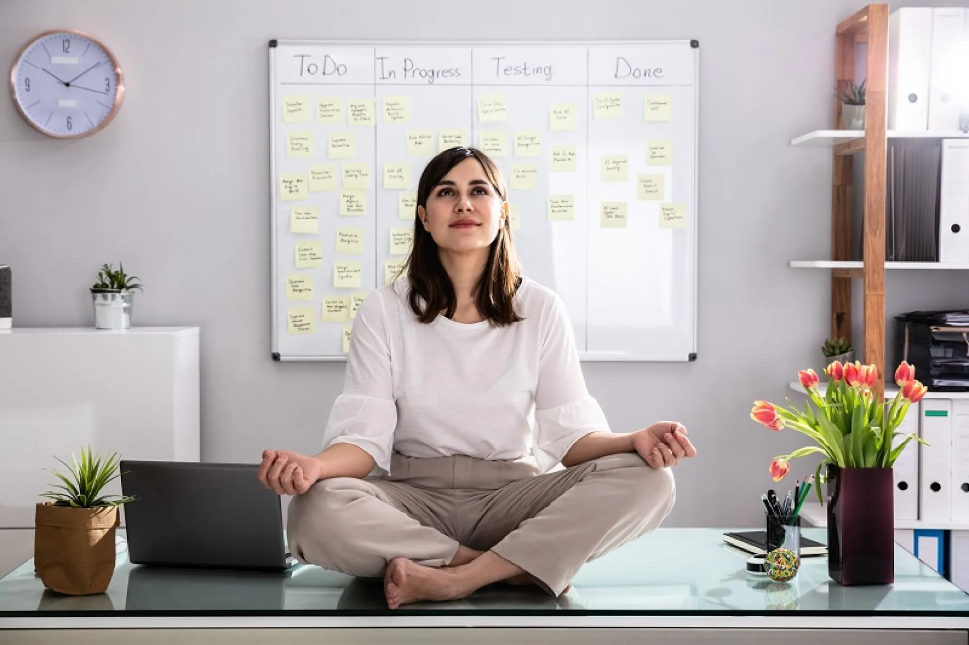 Eine Arbeitnehmerin sitzt auf ihrem Schreibtisch und meditiert, um zu entspannen.