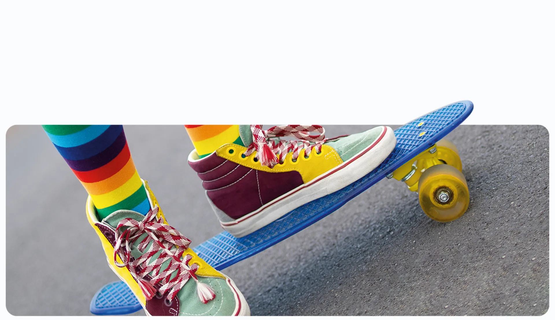 Füße in bunten Schuhen und Socken auf einem Skateboard auf asphaltierter Straße