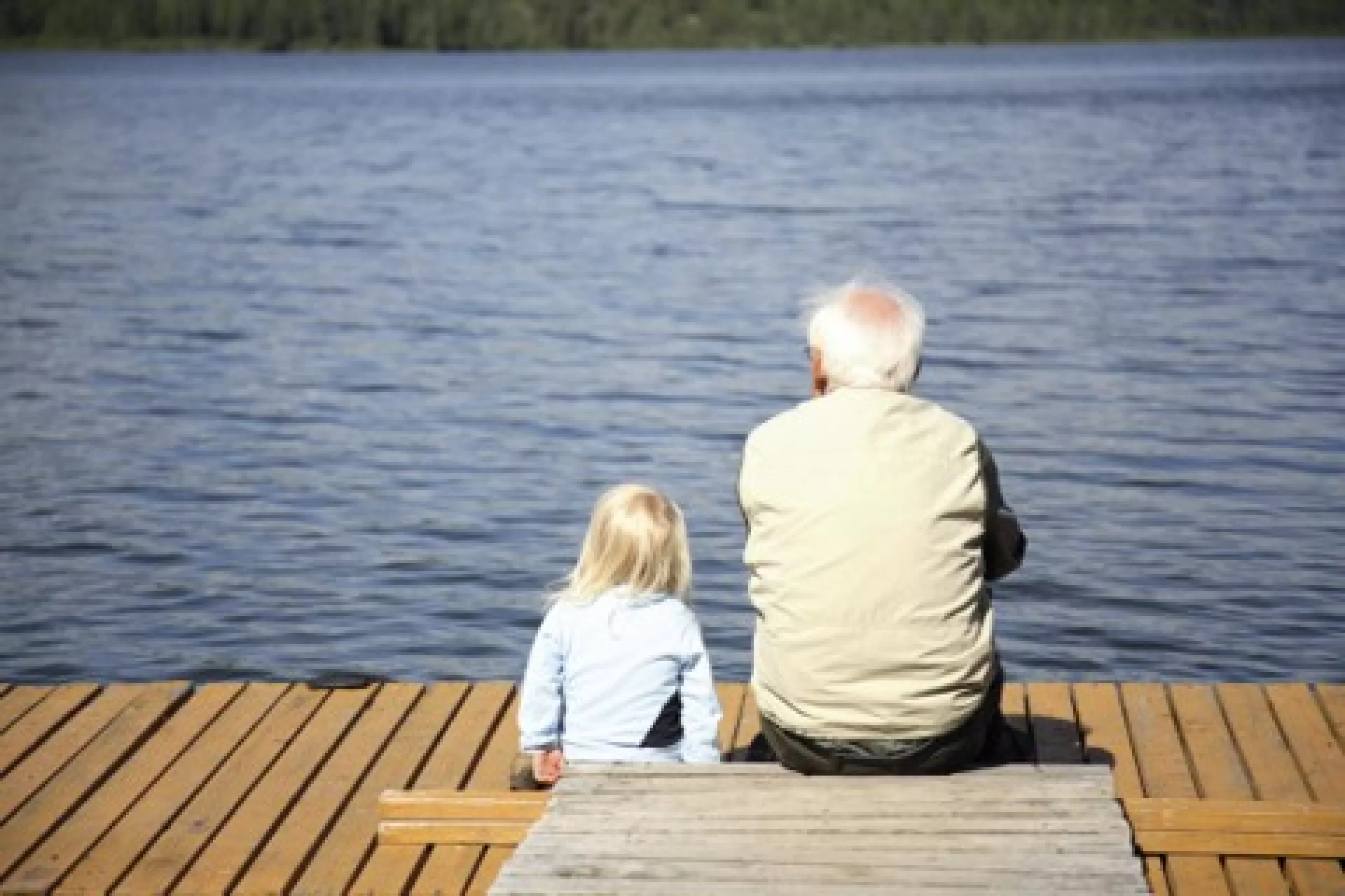 Rückenansicht: Opa und Enkel sitzen auf dem Steg und blicken aufs Wasser