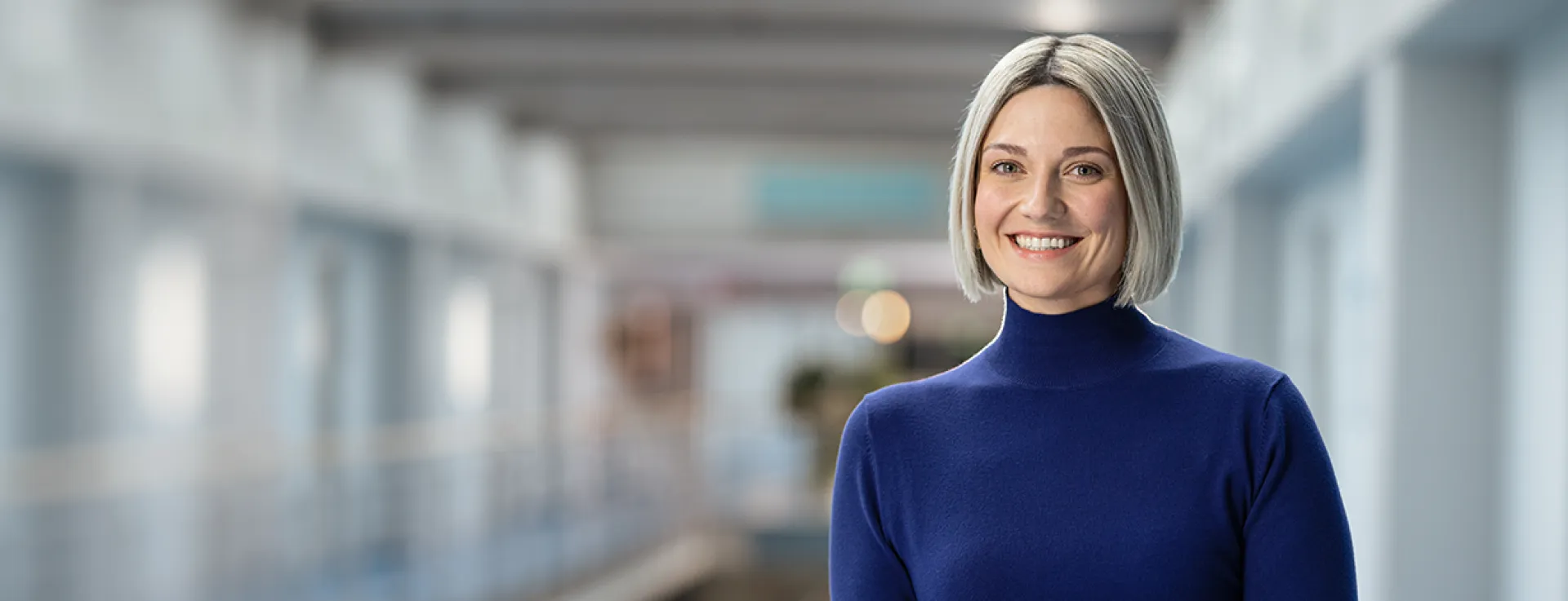 Lächelnde Frau mit kinnlangen hellen Haaren und einem blauen Oberteil