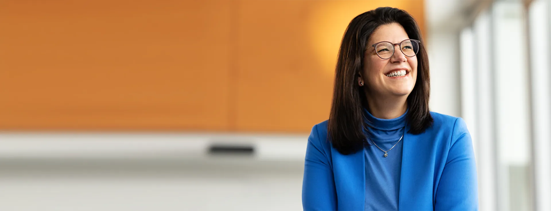 Lächelnde Frau mit schulterlangen Haaren, Brille und blauem Oberteil und Blazer
